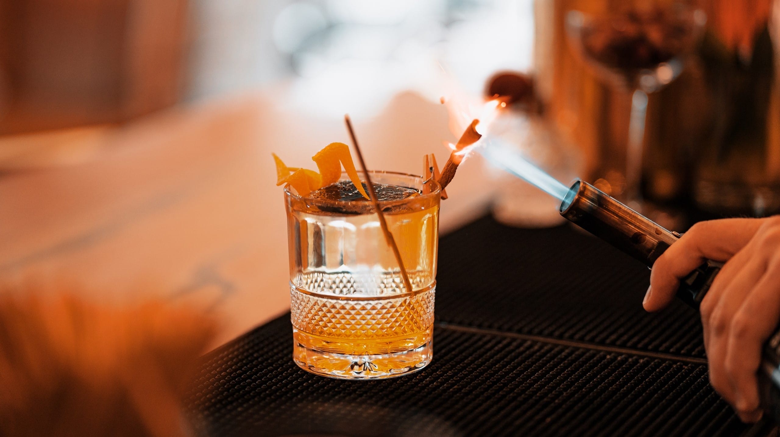 Un cocktail Old Fashioned avec zeste d'orange flambé, servi dans un verre à whisky.